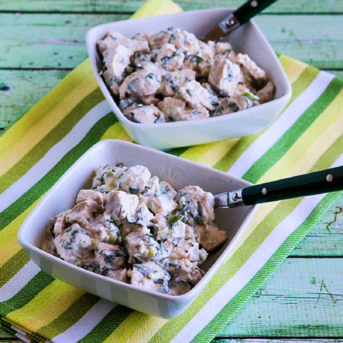 Square image of Chicken Salad with Basil shown in two serving bowls on striped napkin.