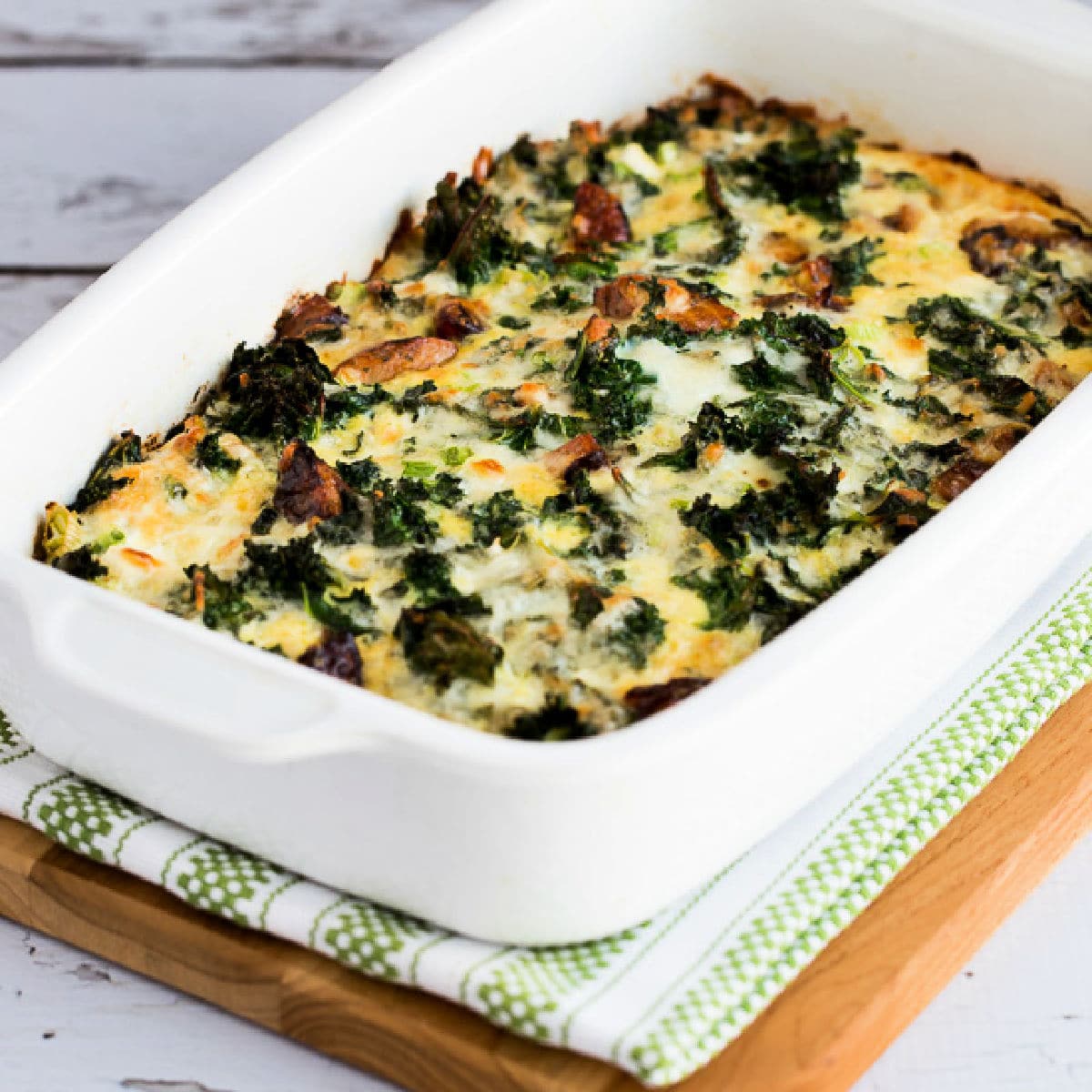 Square image for Sausage, Kale, and Mozzarella Egg Bake shown in baking dish on napkin and cutting board.