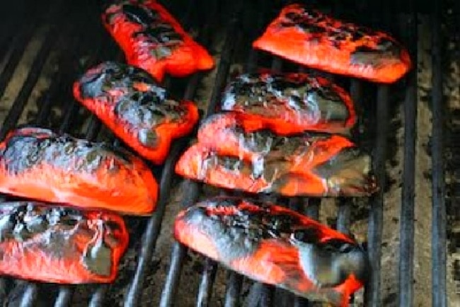 How To Roast Red Peppers (on the grill) photo of charred peppers on the grill grates.