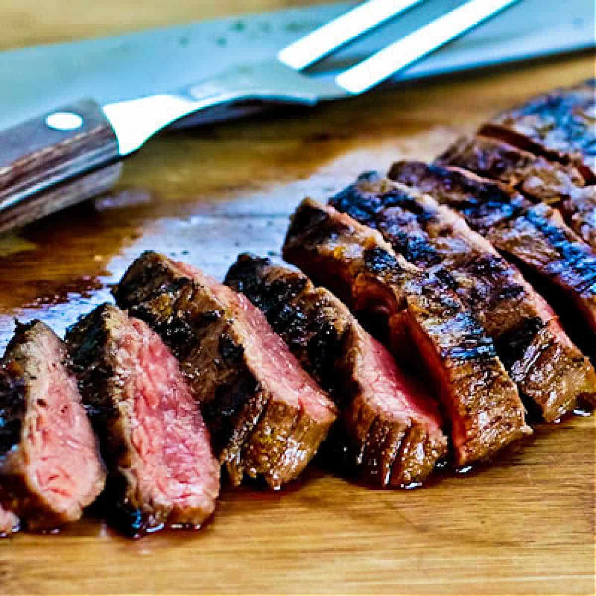Grilled Cuban Flank Steak shown on cutting board with knife and fork.
