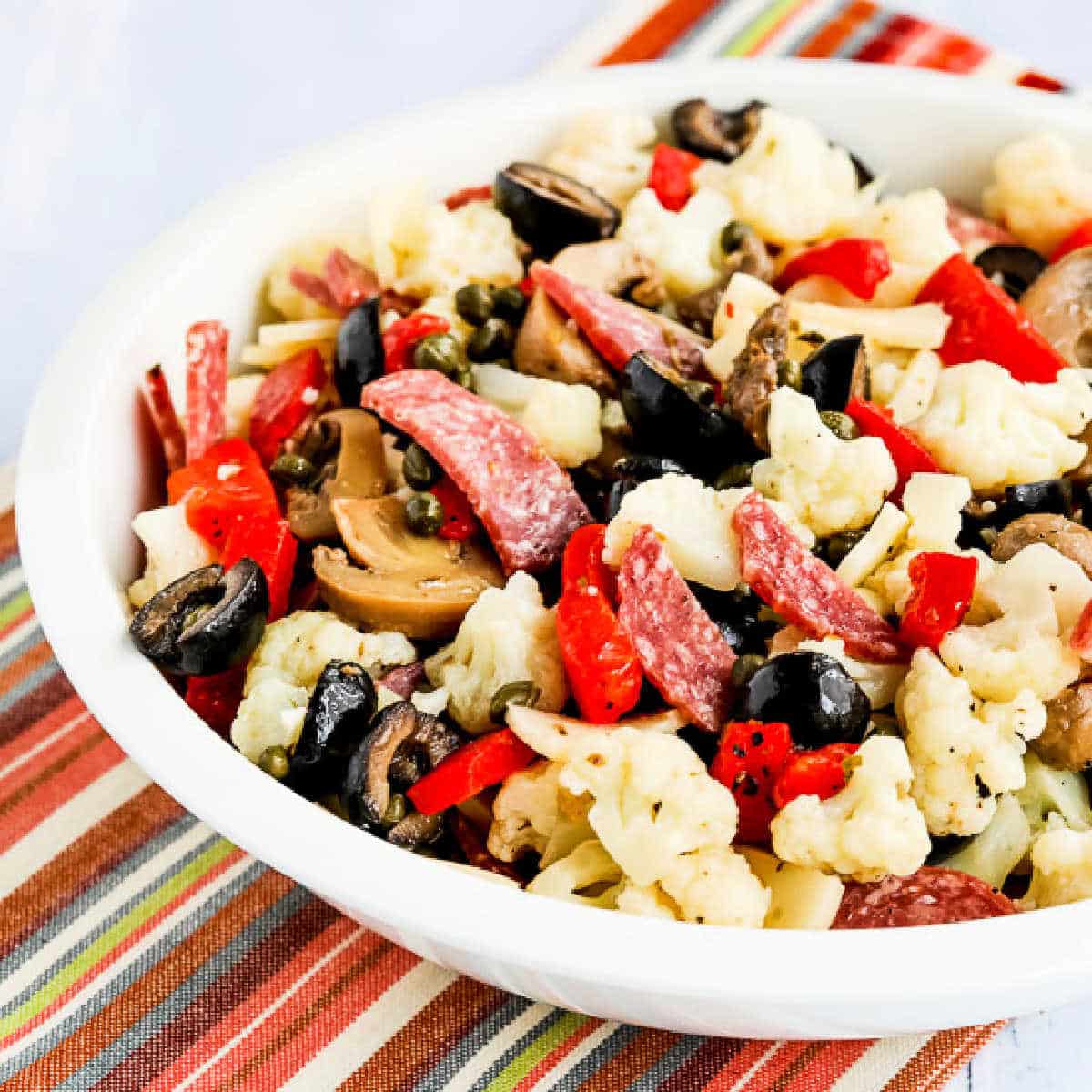 Marinated Cauliflower Antipasto Salad shown in serving bowl on striped napkin.