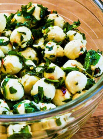 Square image of marinated fresh mozzarella with chopped herbs.