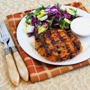 Square image of Grilled Salmon Burgers with Caper Mayo shown on serving plate with salad, on napkin.