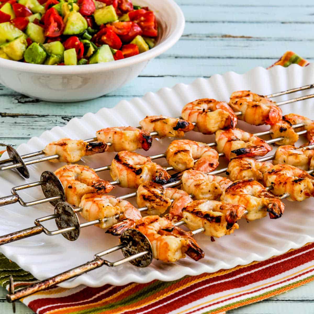 Square image of Grilled Shrimp Skewers on serving platter with black bean salsa in back.
