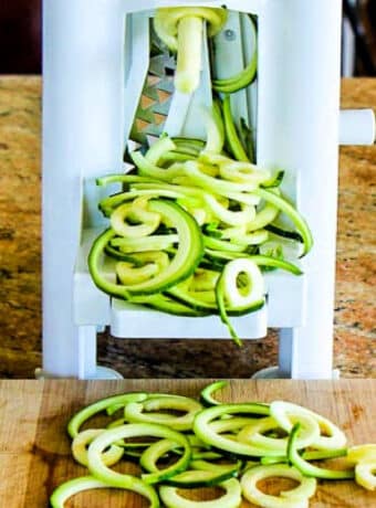 How to Make Zucchini Noodles photo showing spiralizer with zoodles on cutting board.
