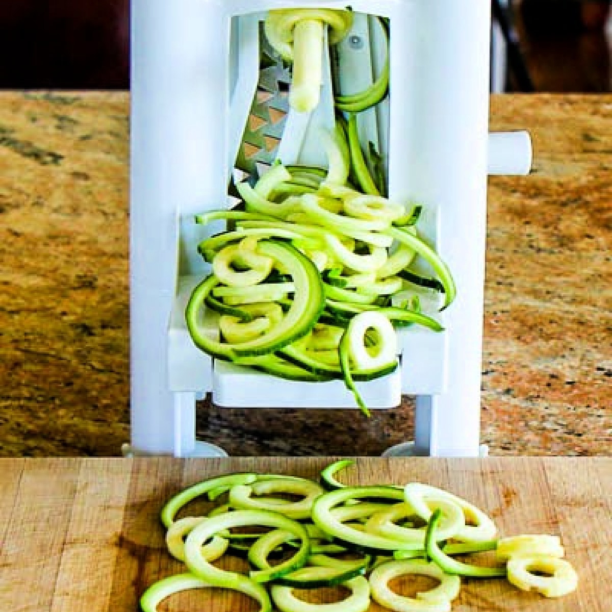 How to Make Zucchini Noodles photo showing spiralizer with zoodles on cutting board.