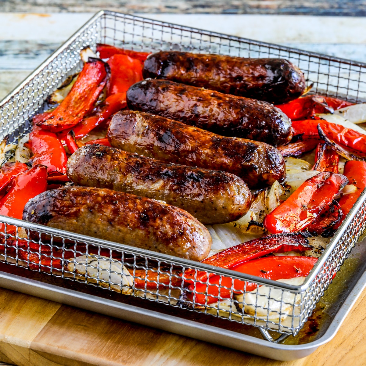 Square image of air fryer sausages and peppers in air fryer basket