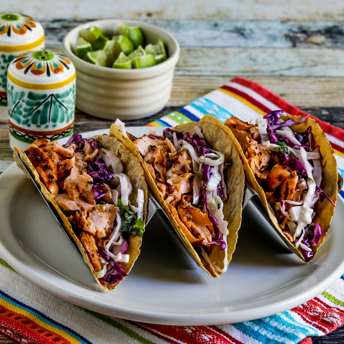 salmon tacos with Mexican slaw shown in taco holder on serving plate, with limes in background