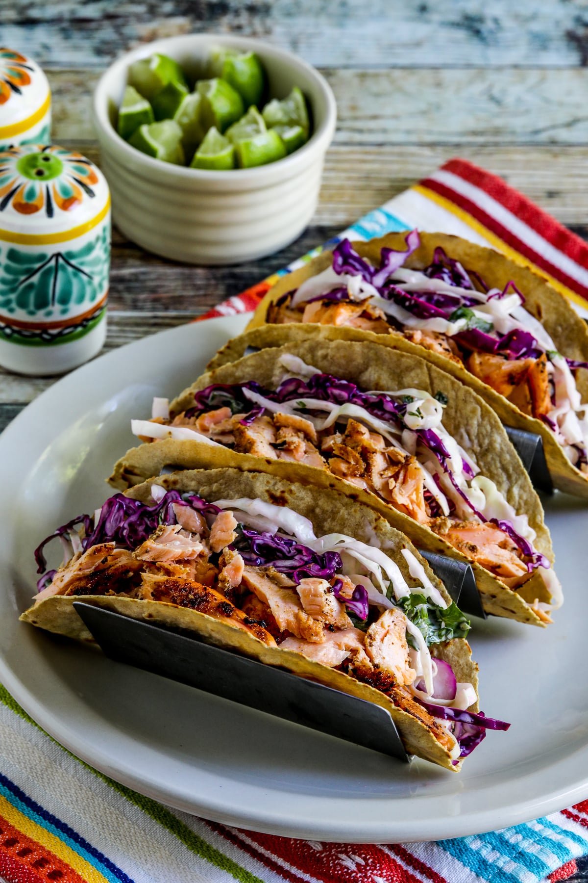 Salmon taco with mexican slaw displayed in a taco stand with limes on the side