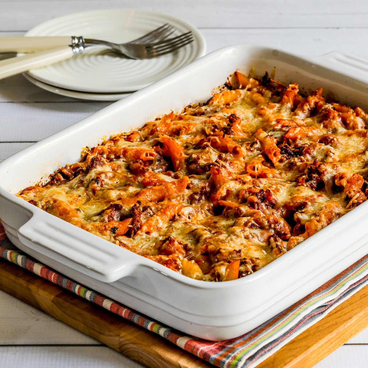 Baked penne with sausages in a square image of a casserole in a baking dish