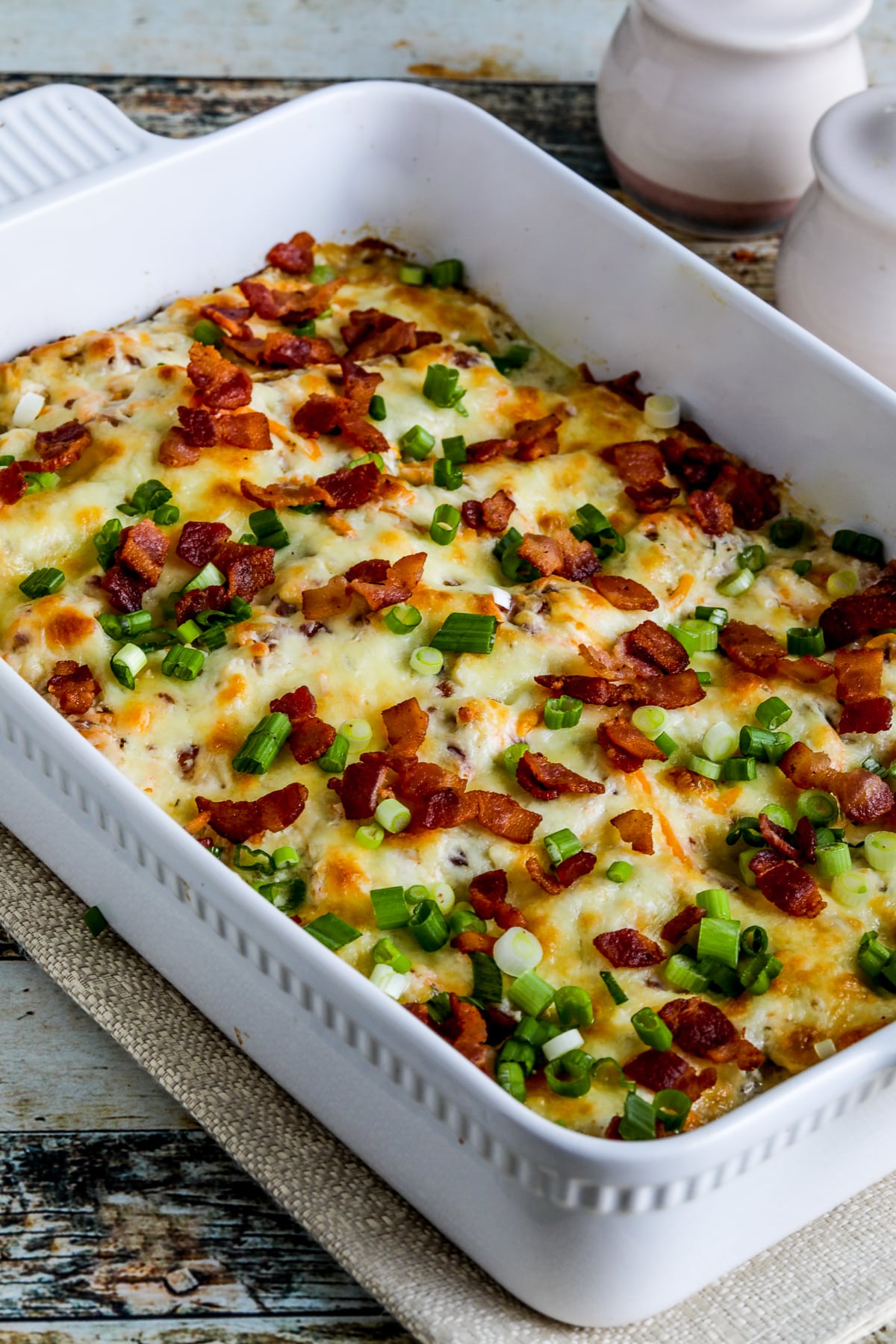 Keto Crack Chicken Bake shown in baking dish with bacon and green onion sprinkled on