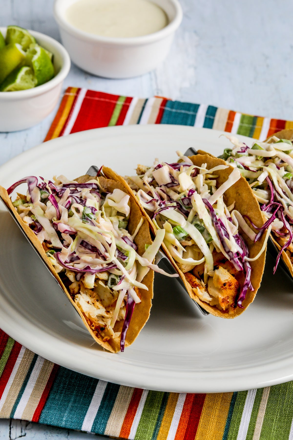 Three Air Fryer Fish Tacos shown in taco holder with extra sauce in background