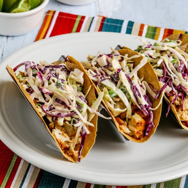 Air Fryer Fish Tacos shown on taco rack with limes and extra sauce in background