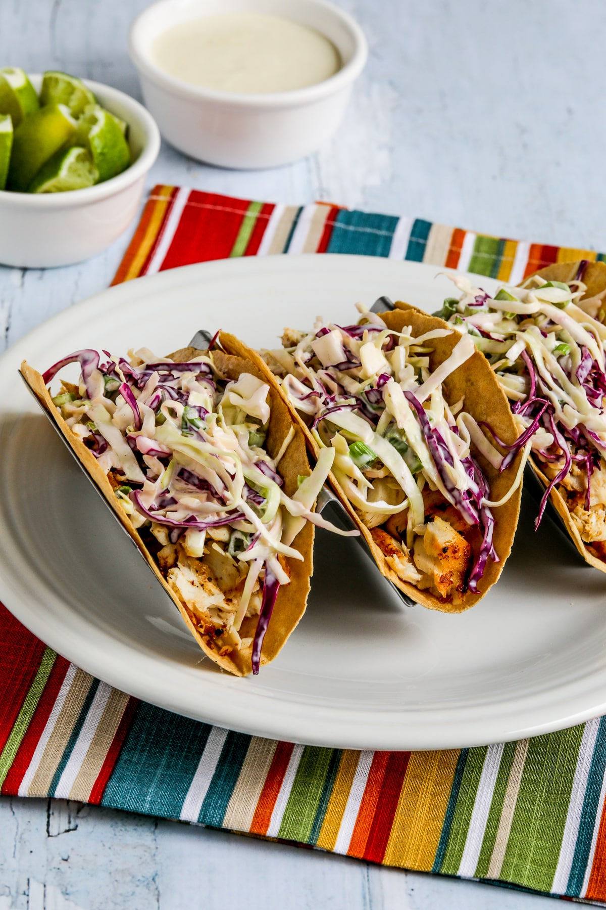 Air fryer fish tacos displayed on a taco rack with lime and additional sauce in the background
