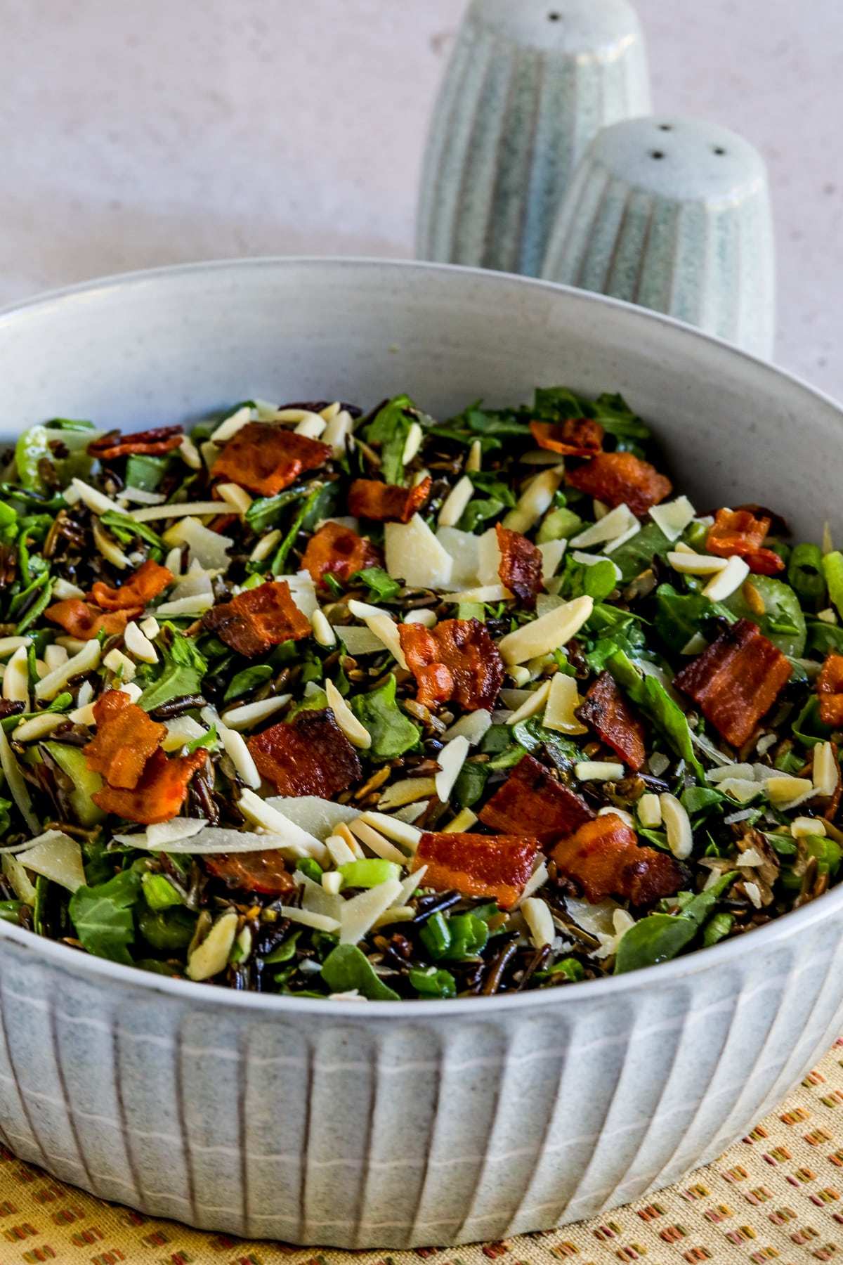 Wild Rice Salad with Bacon and Arugula shown in bowl with salt-pepper in back.