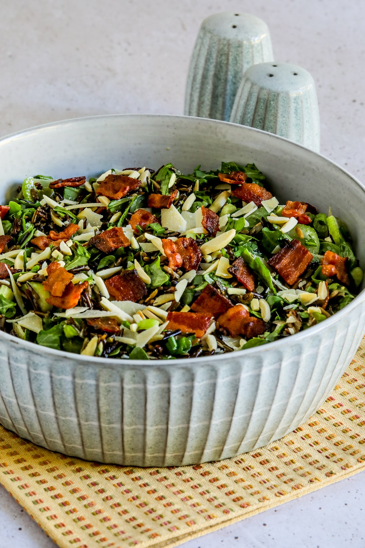Farther back image for Wild Rice Salad with Bacon and Arugula shown in bowl with salt-pepper in back.