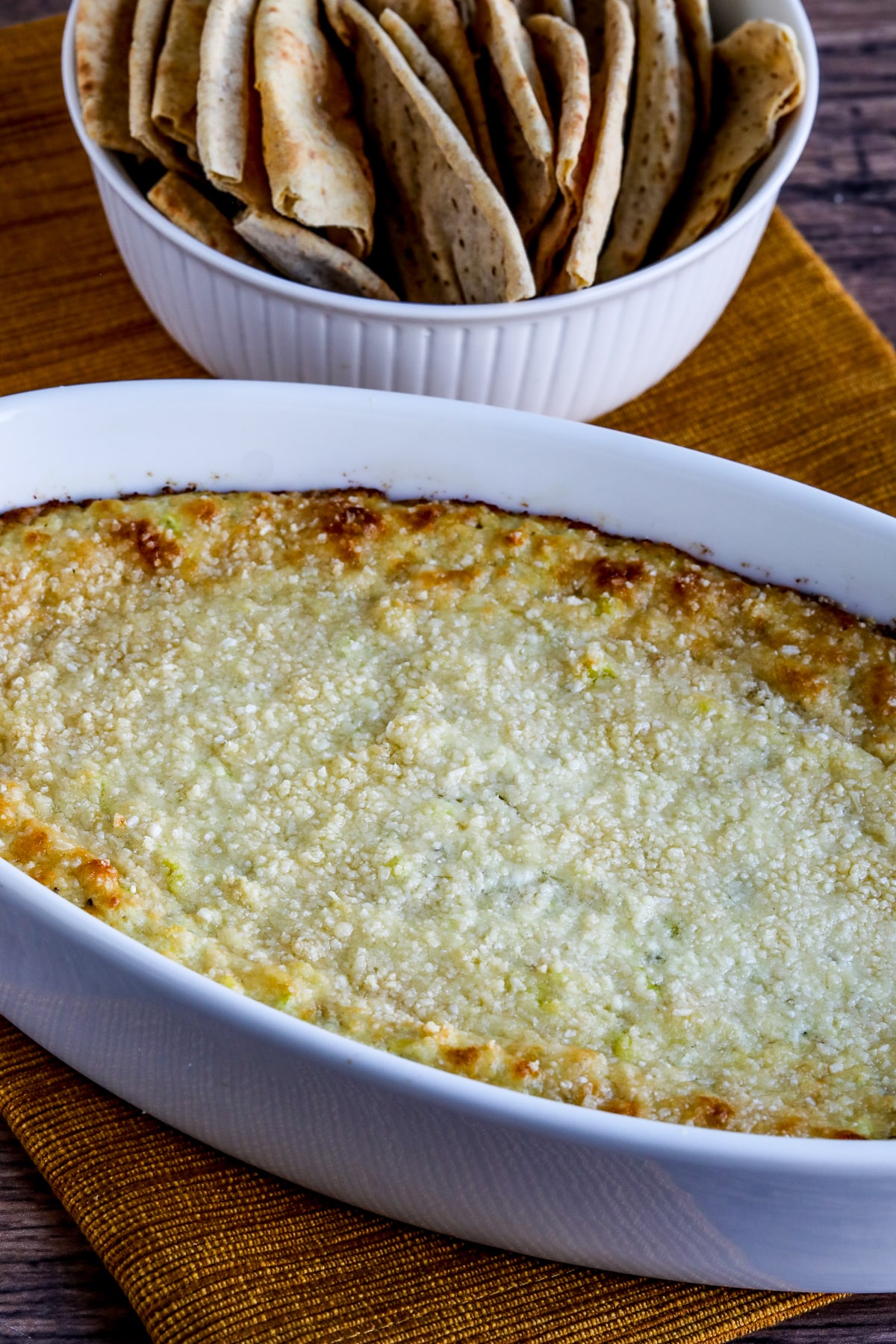 Hot Artichoke Dip (with Peperoncini) shown in bowl with toasted low-carb pita bread in back.
