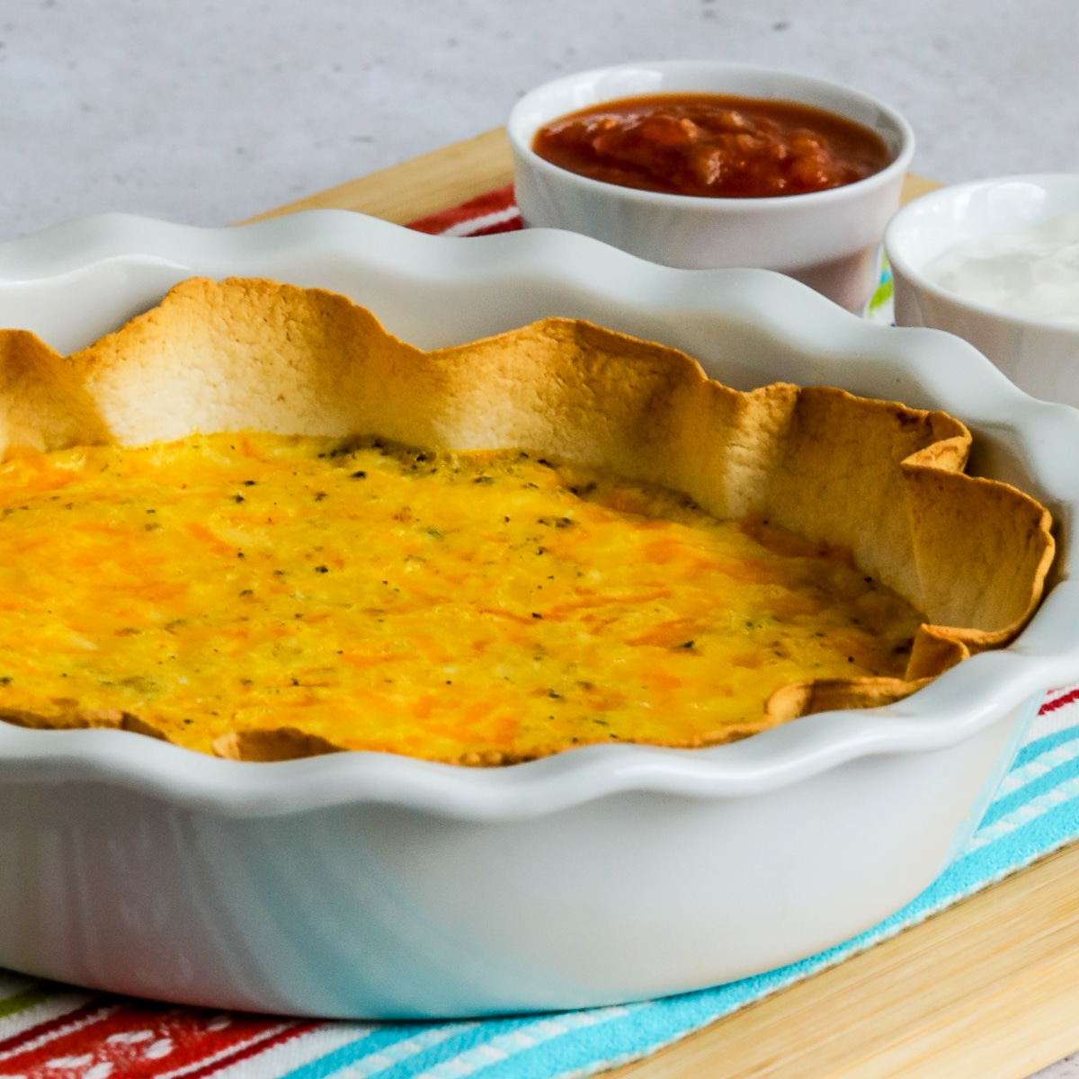 Square image for Tortilla Egg Bake in pie plate with sour cream and salsa on the side.