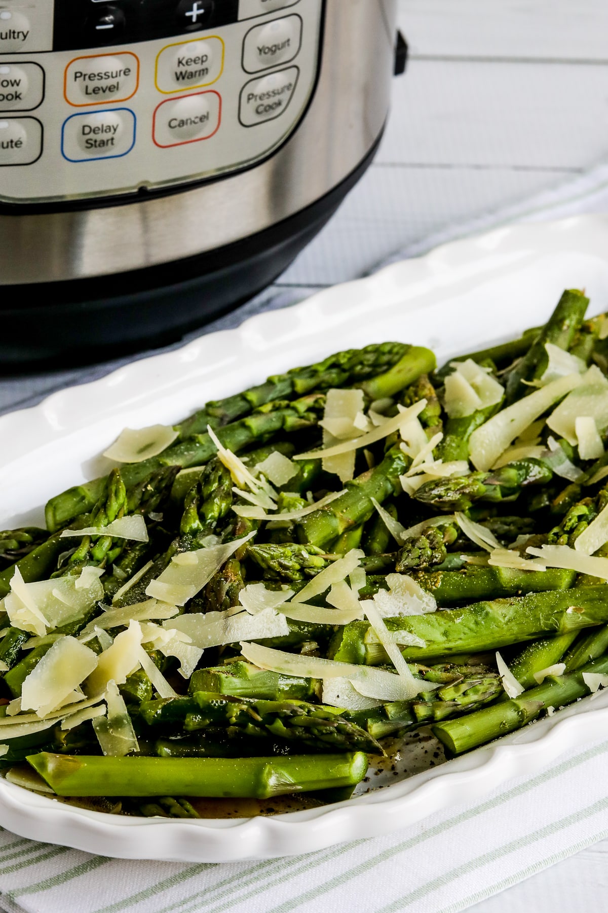 Instant Pot Asparagus shown with asparagus with browned butter and Parmesan on platter and Instant Pot in back.
