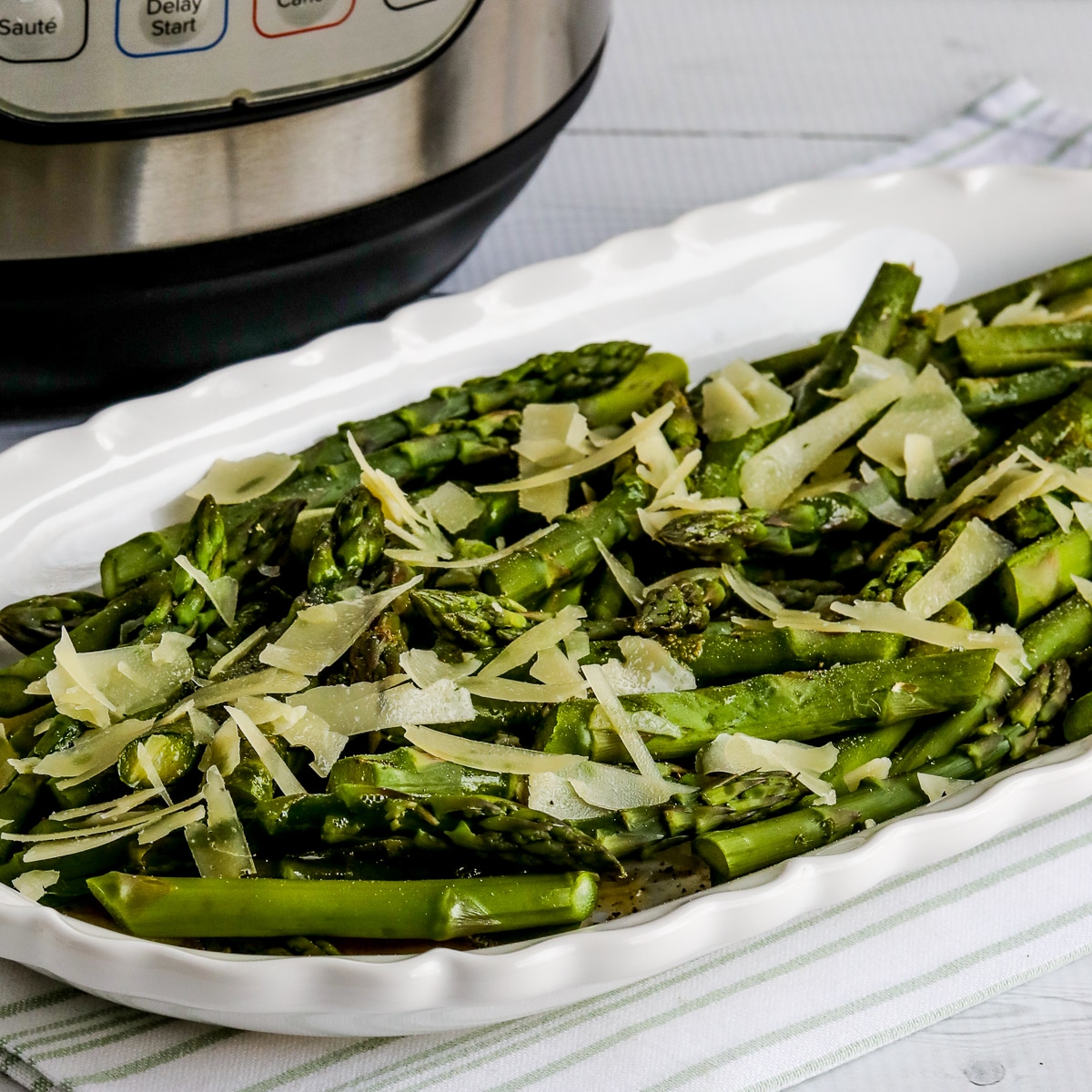 Instant Pot Asparagus shown on serving plate with butter and Parmesan and Instant Pot in back.