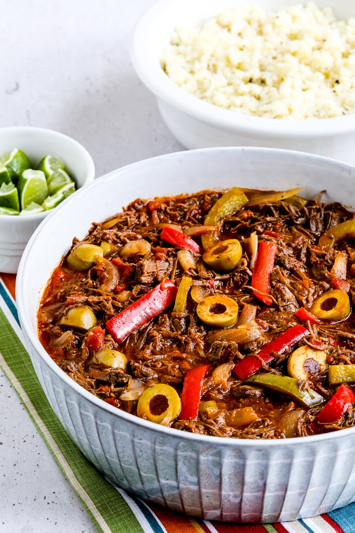 Ropa Vieja Recipe shown in serving bowl with side dish and limes.