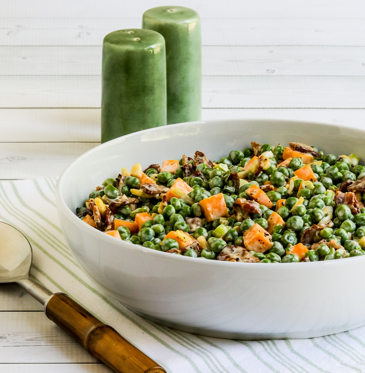 Bacon and Pea salad shown in white serving bowl with fork and salt-pepper shakers.