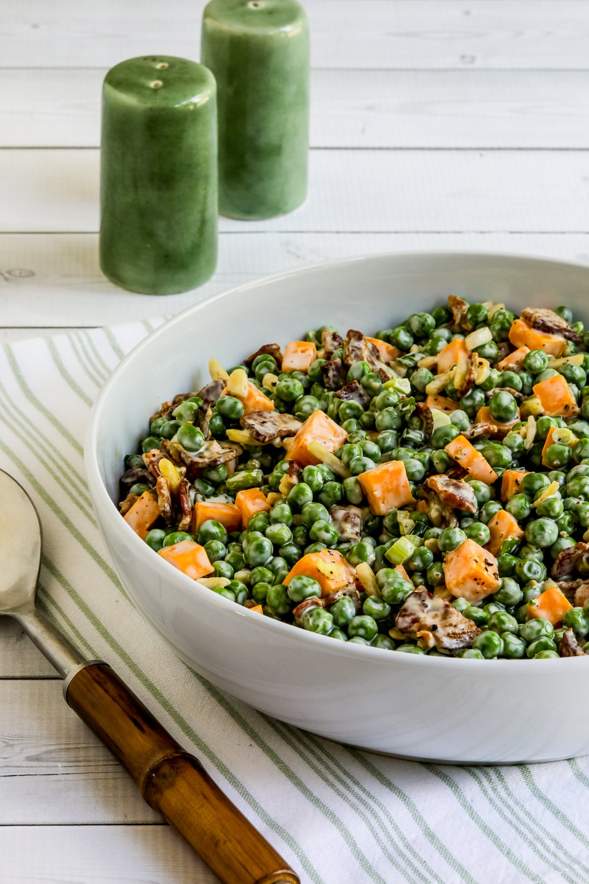 Vertical image of Bacon and Pea Salad in bowl with serving spoon and salt-pepper shakers.