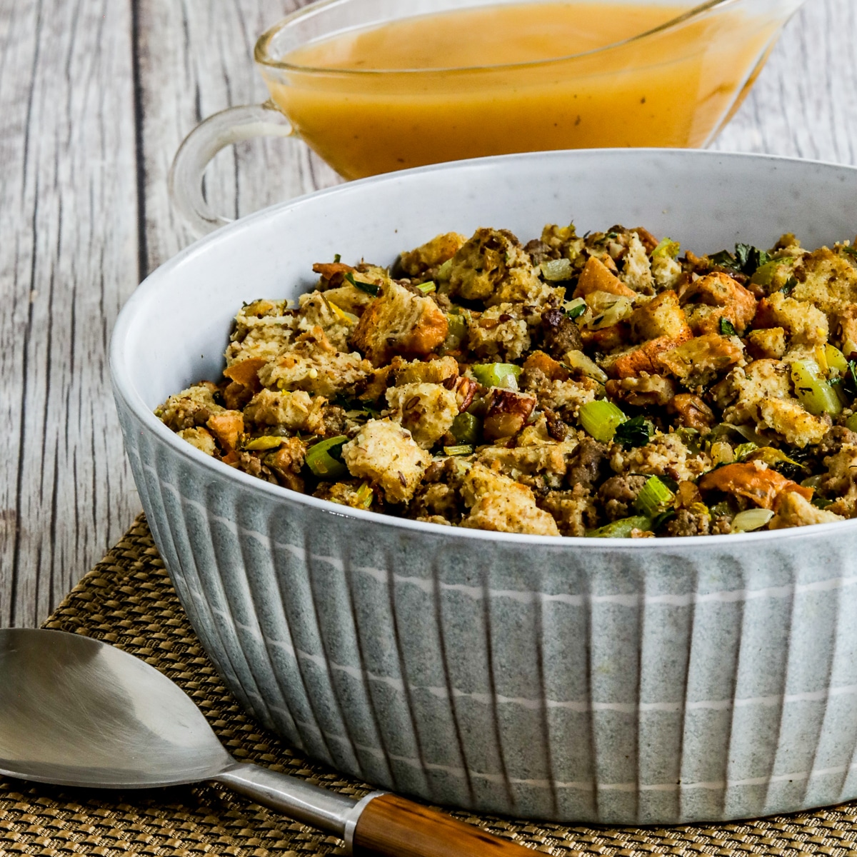 Low-Carb Stuffing (with Sausage and Pecans), square image of stuffing in serving dish with spoon on side and gravy in back.