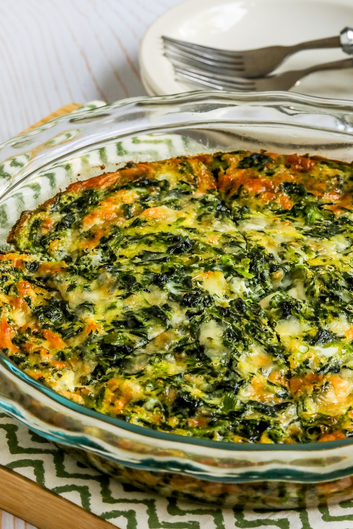 Crustless Spinach Quiche shown in baking dish with slices cut and plates/forks in back.