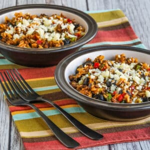 Square image of two Slow Cooker Beef Taco Bowls with forks on colorful napkin.