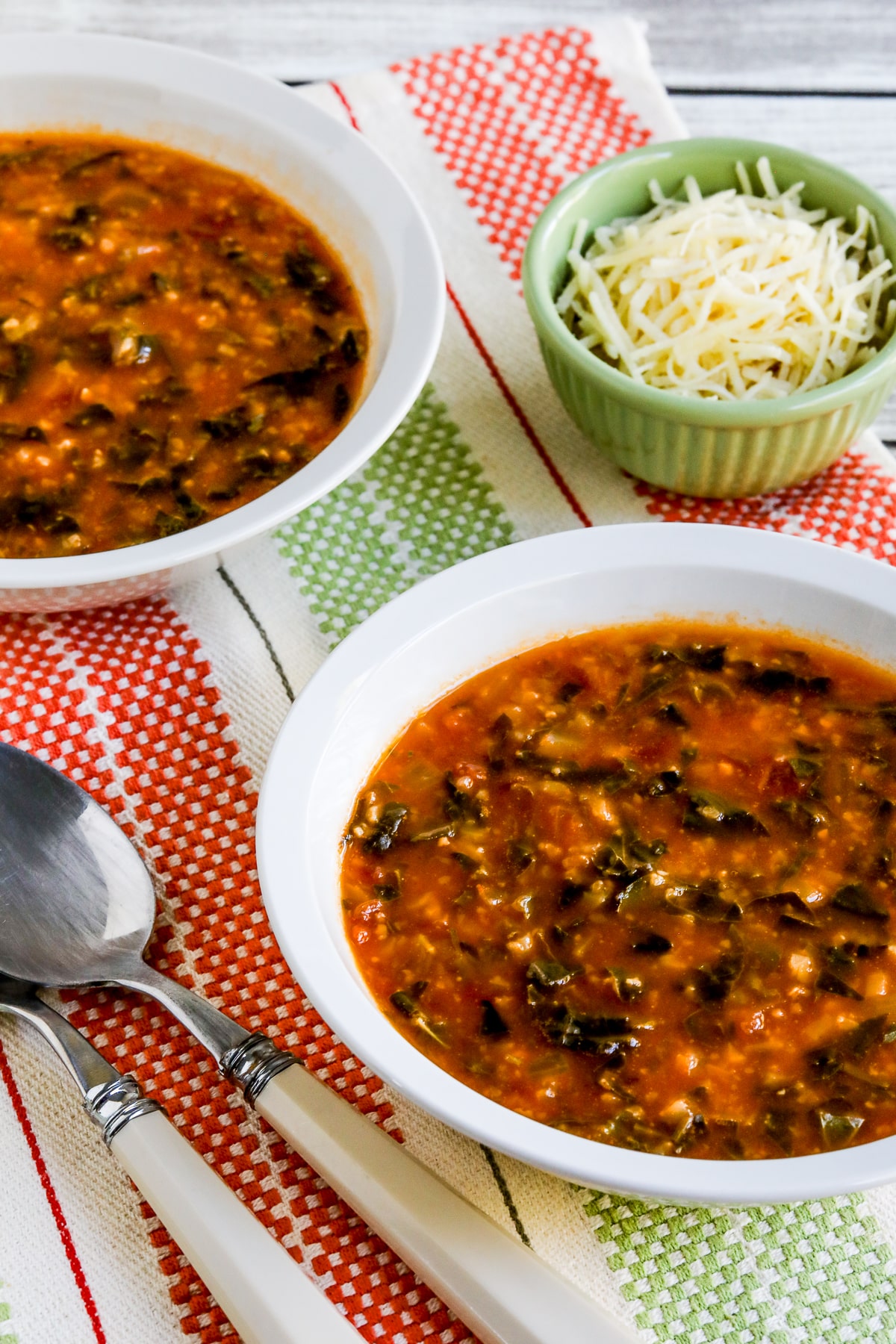 Tomato Spinach Soup shown in two bowls with Parmesan cheese and spoons.