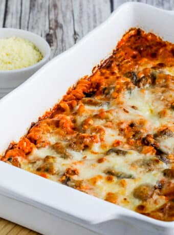 Square featured image for Cottage Cheese Pasta Bake with Mushrooms shown in baking dish with Parmesan in back.